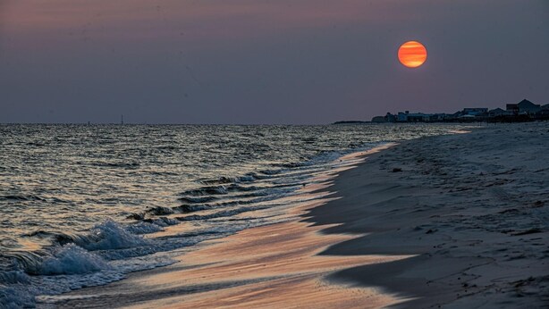 Een strand bij zonsondergang, met zachte golven die op het strand spoelen.