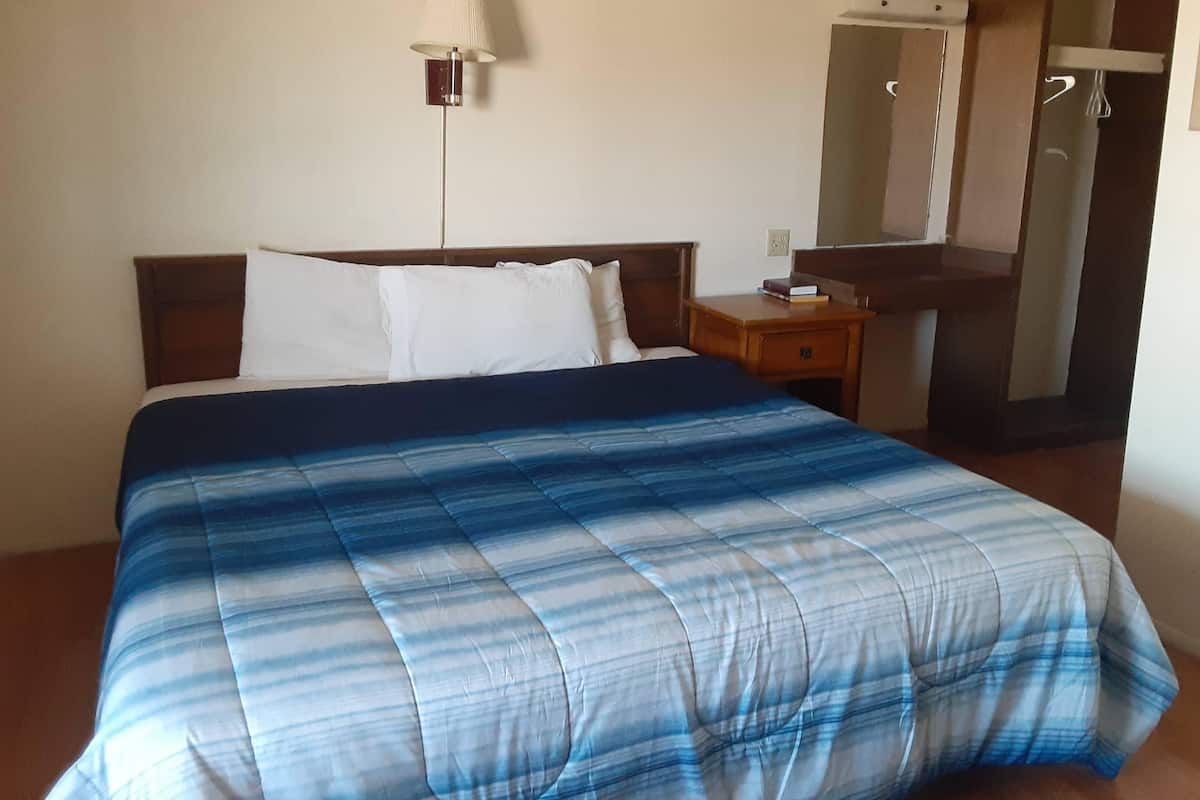 A hotel room with a bed, a bedside table, a lamp, and a mirror.