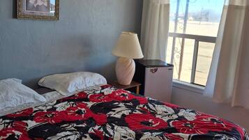 Un dormitorio con colcha estampada, un cuadro enmarcado en la pared, una lámpara de noche y una ventana con cortinas.