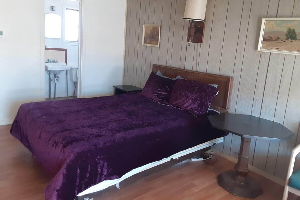 A bedroom with a wooden bed, a bedside table, a lamp, and a small desk with a chair.