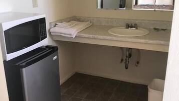 Una kitchenette compacta con microondas, un refrigerador pequeño, un lavamanos y piso de baldosas.