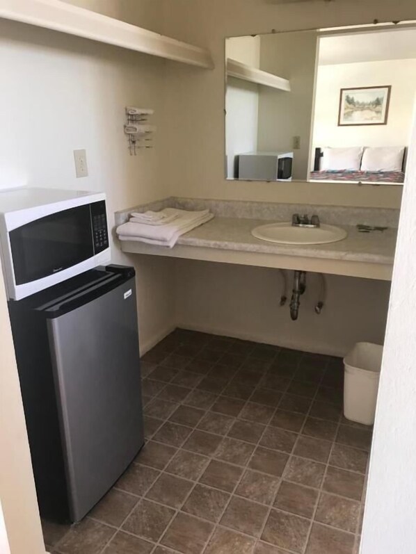 Una kitchenette compacta con microondas, un refrigerador pequeño, un lavamanos y piso de baldosas.