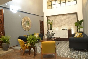 A modern lobby with a reception desk, seating area with sofas and chairs, decorative wall art, and potted plants.