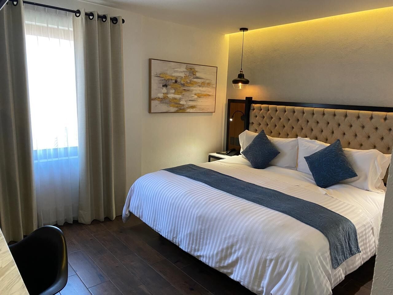 Een hotelkamer met een groot bed, nachtkastje, lamp en raam met gordijnen.