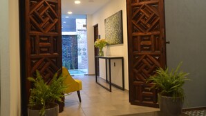 A wooden door leading to a hallway with a potted plant, a yellow chair, and a console table with a vase of flowers. - Hotel Boutique Casa Loreta (Querétaro)