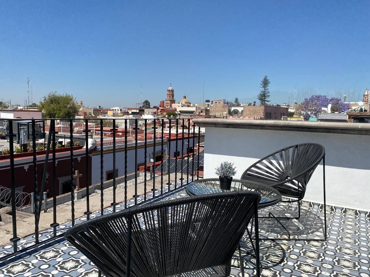 Une terrasse avec deux chaises en osier noir et une petite table, donnant sur une rivière avec des bâtiments en arrière-plan.