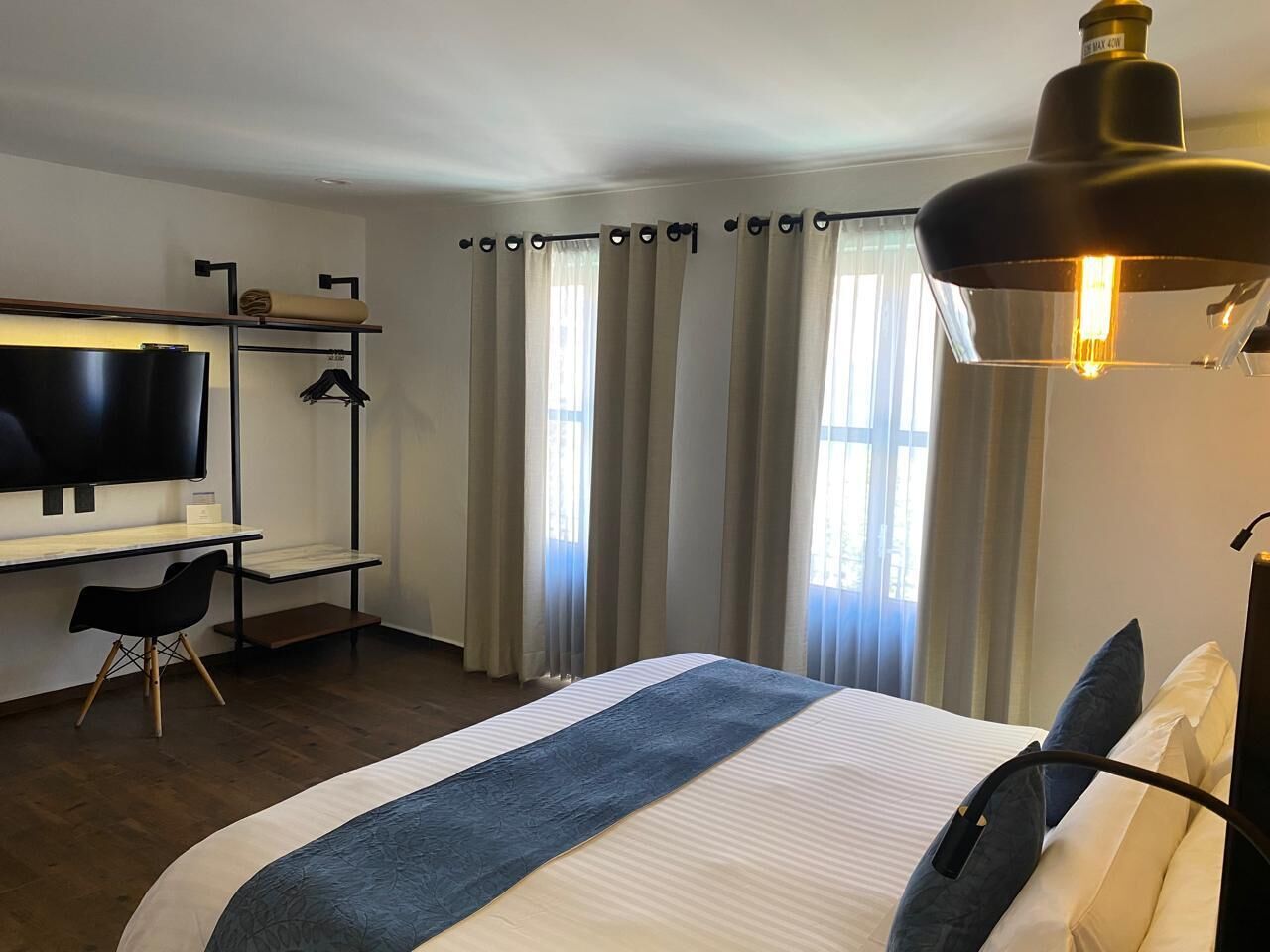 A hotel room with a bed, a desk, a chair, a TV, and a window with curtains.
