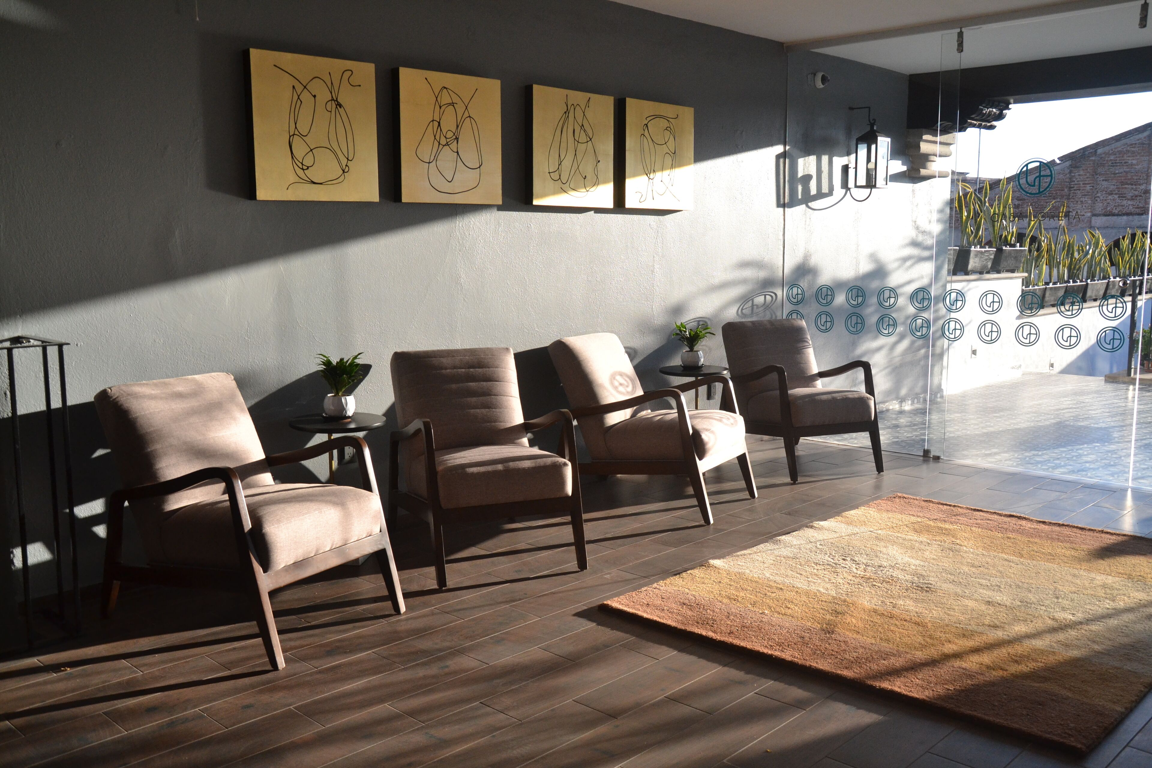 A modern living room with four leather armchairs, a coffee table, and a rug. There are abstract paintings on the wall and a potted plant on the coffee table.