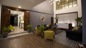 A modern lobby with a dark blue sofa, yellow chairs, wooden decor, and a patterned floor. - Hotel Boutique Casa Loreta (Querétaro)