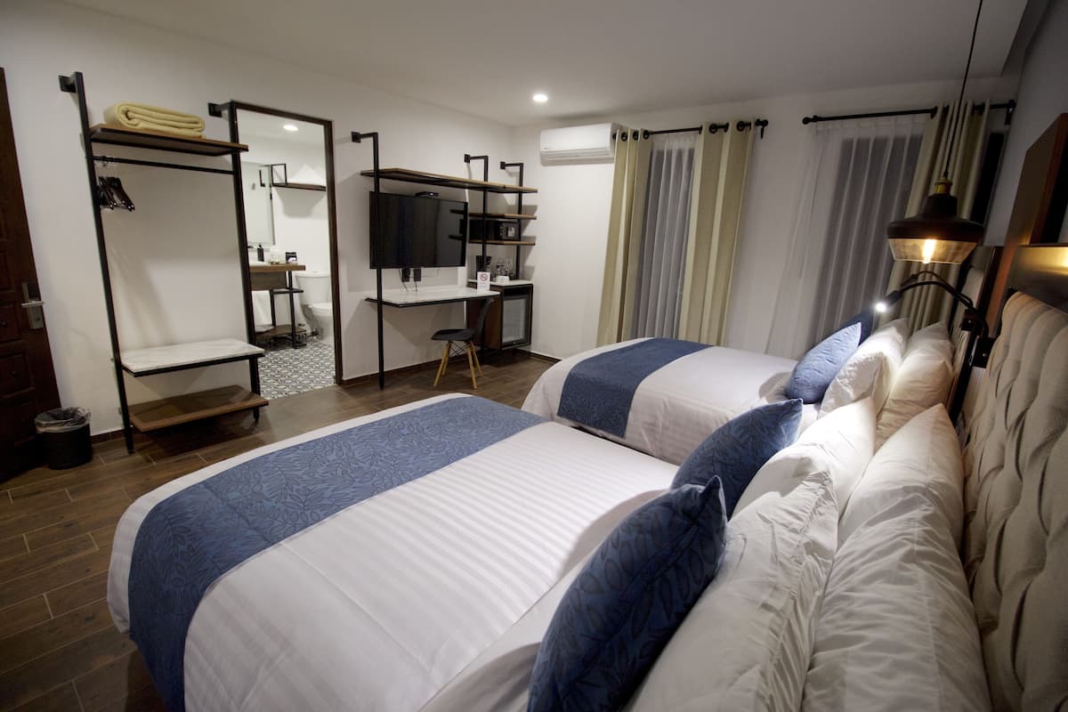 Une chambre d’hôtel avec deux lits, un bureau avec un ordinateur, une télévision et un appareil de climatisation.