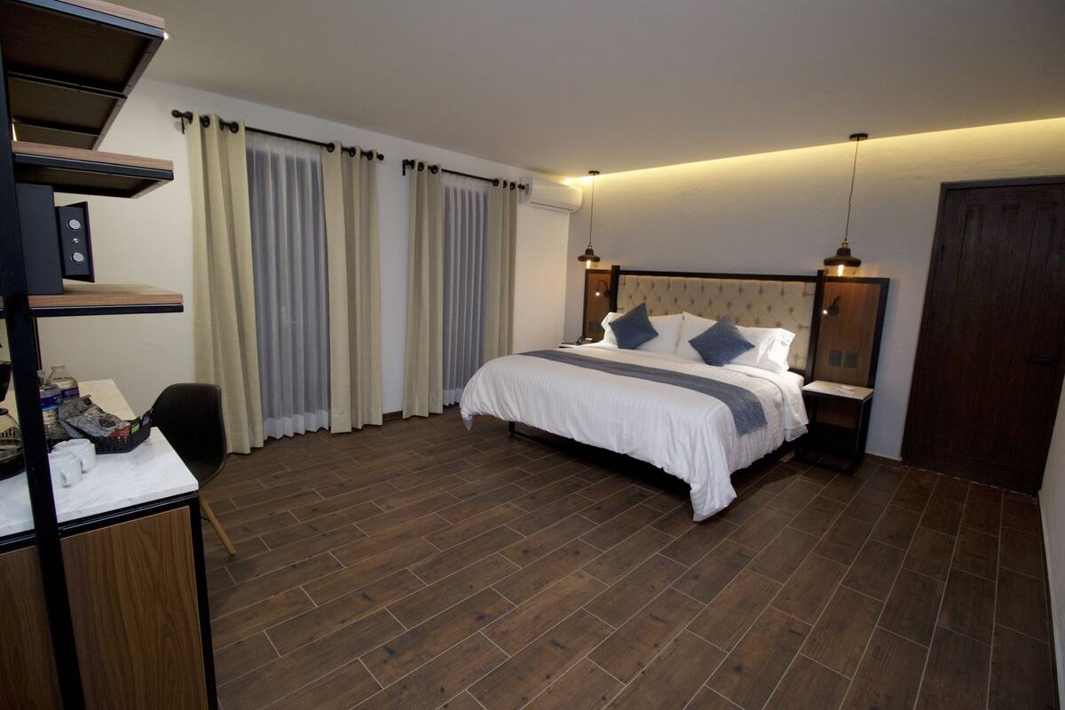Une chambre à coucher avec un lit, un plancher en bois, des rideaux, un bureau avec une chaise et une armoire.