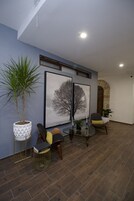 Una sala de estar moderna con una planta grande en maceta, dos cuadros enmarcados, una mesa de centro de vidrio y un sillón cómodo.