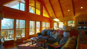 Una cabaña espaciosa con ventanas amplias, una zona de estar acogedora con sofá y chimenea, y una cocina equipada con electrodomésticos modernos.