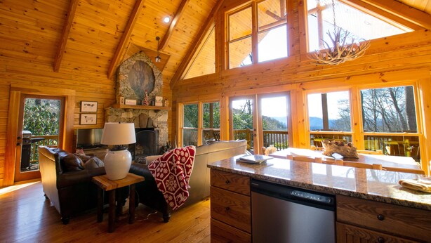 Interior de una cabaña de madera con cocina, comedor y chimenea de piedra.