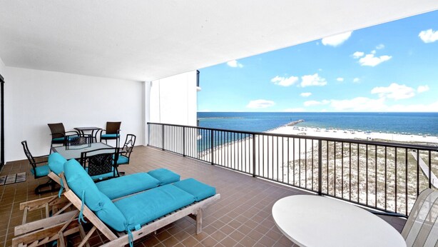 A balcony with a view of the beach, a table, chairs, and a lounge area with blue cushions. - Grand Pointe 610 | Amazing Views of Perdido Pass | Beachfront Condo | My Beach Getaways (Orange Beach)