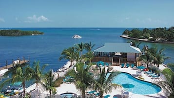 Relax by the resort's curved pool, surrounded by lounge chairs and umbrellas, with a restaurant or communal area nearby.