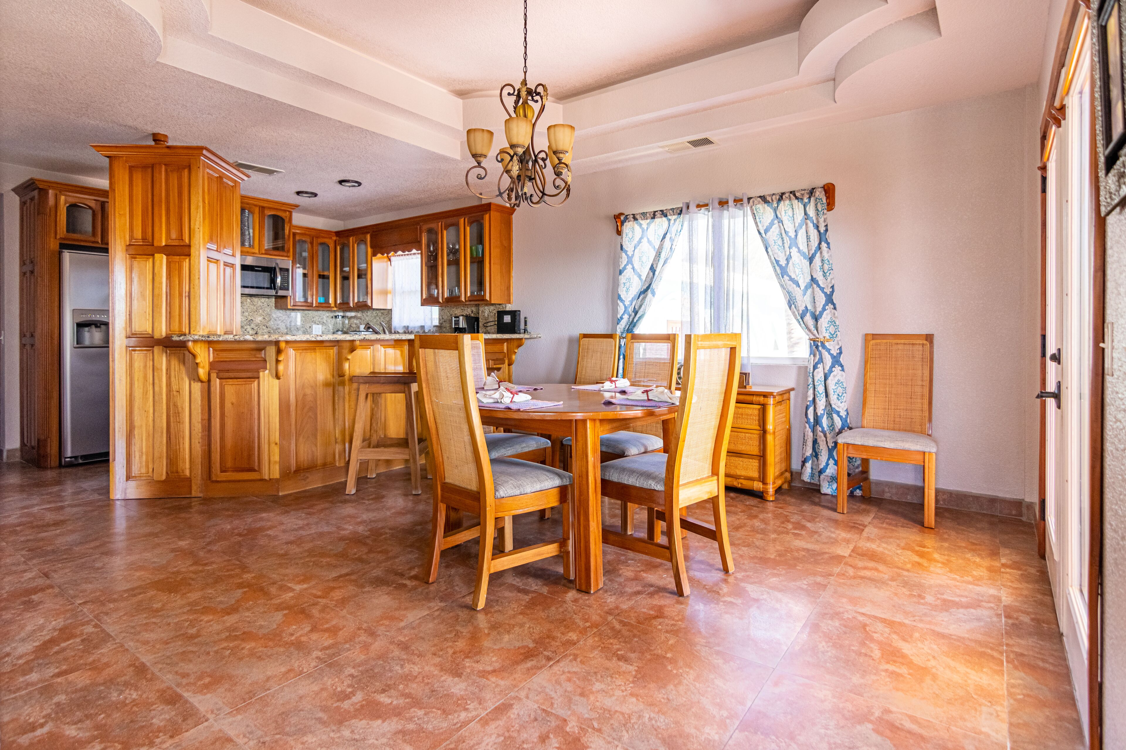 A spacious kitchen with wooden cabinets, a central island, and a dining area with chairs and a table.