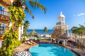 A resort with a swimming pool, lounge chairs, and a view of the ocean. - Lighthouse Beach Villas (San Pedro)