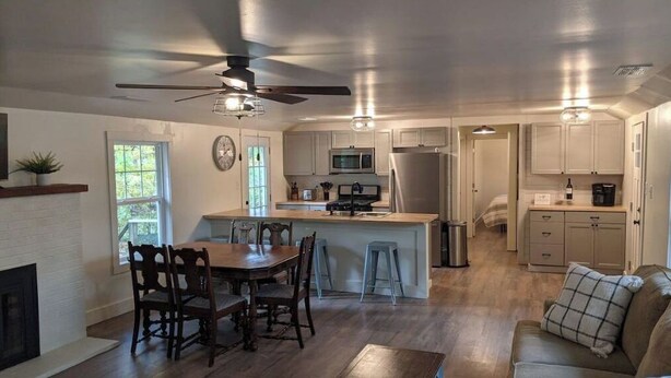 A modern kitchen with a central island, wooden dining table, and chairs. There is a ceiling fan, a microwave, and a refrigerator. - NEW! Beautiful Riverfront Home on 10 Acres! (Chesterton)