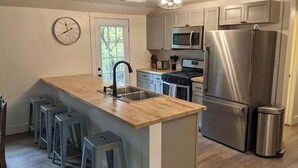 A modern kitchen with a central island, stainless steel appliances, and a clock on the wall. - NEW! Beautiful Riverfront Home on 10 Acres! (Chesterton)