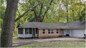 A two-story house with a porch, a garage, and a wooded backdrop. - NEW! Beautiful Riverfront Home on 10 Acres! (Chesterton)