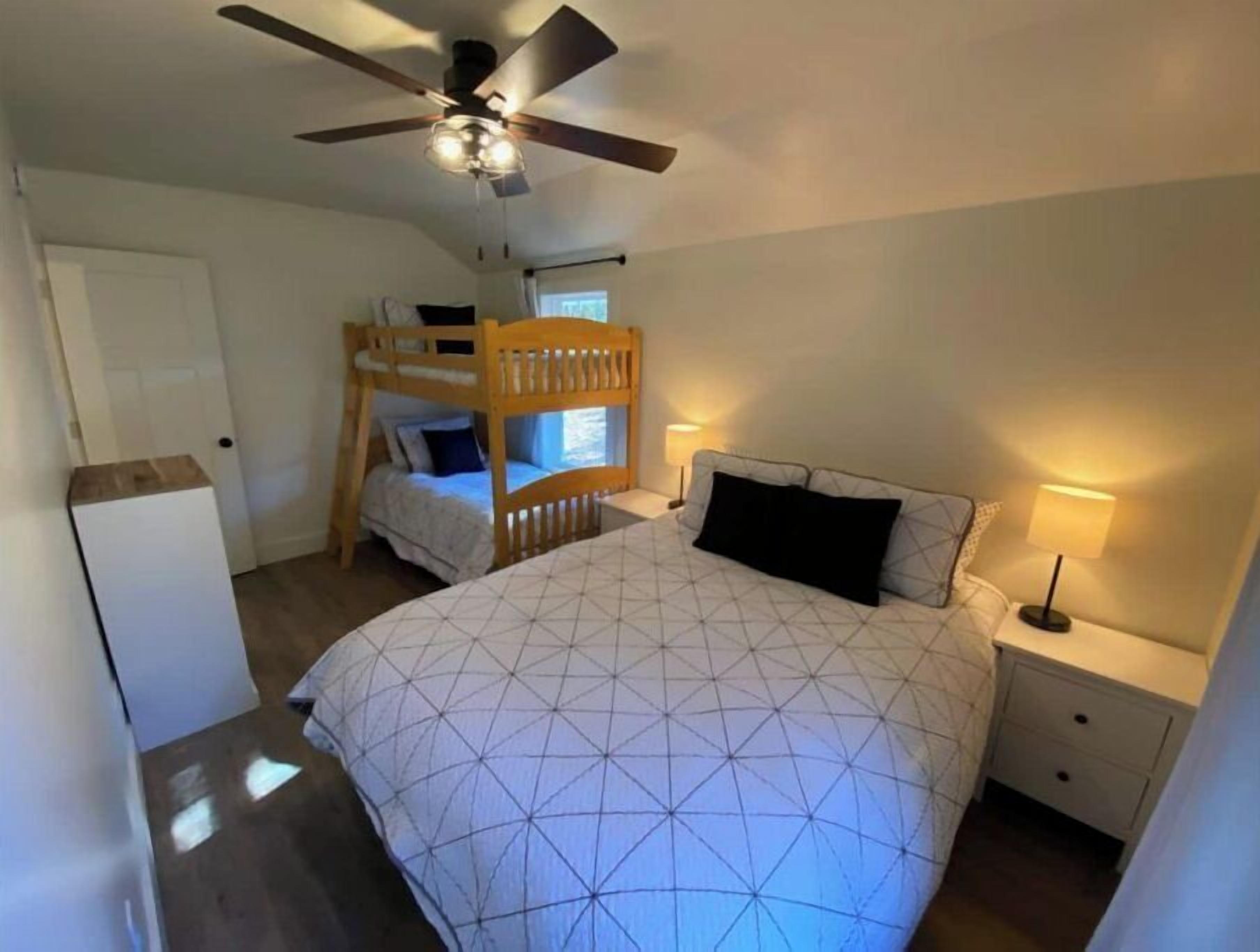 Ein Schlafzimmer mit Etagenbett, einem Einzelbett, einem Deckenventilator, einem Nachttisch mit Lampe und einem weißen Kleiderschrank.