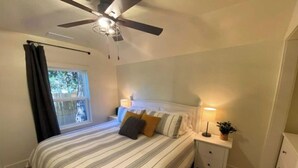 A bedroom with a bed, a nightstand, a ceiling fan, a window with curtains, and a view of greenery outside. - NEW! Beautiful Riverfront Home on 10 Acres! (Chesterton)