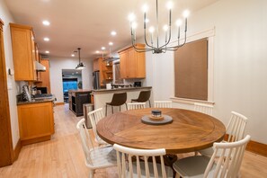 A modern kitchen with wooden cabinets, a round dining table with white chairs, and a chandelier.