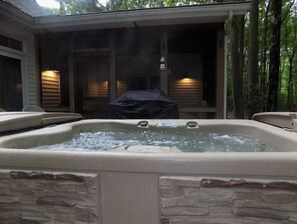 Un bain à remous situé dans un espace extérieur abrité, agrémenté d’éléments en pierre et doté d’une terrasse en bois.