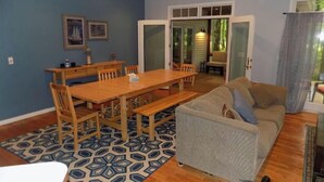 Una sala de estar con una mesa de comedor de madera, sillas, un sofá gris y un tapete estampado.