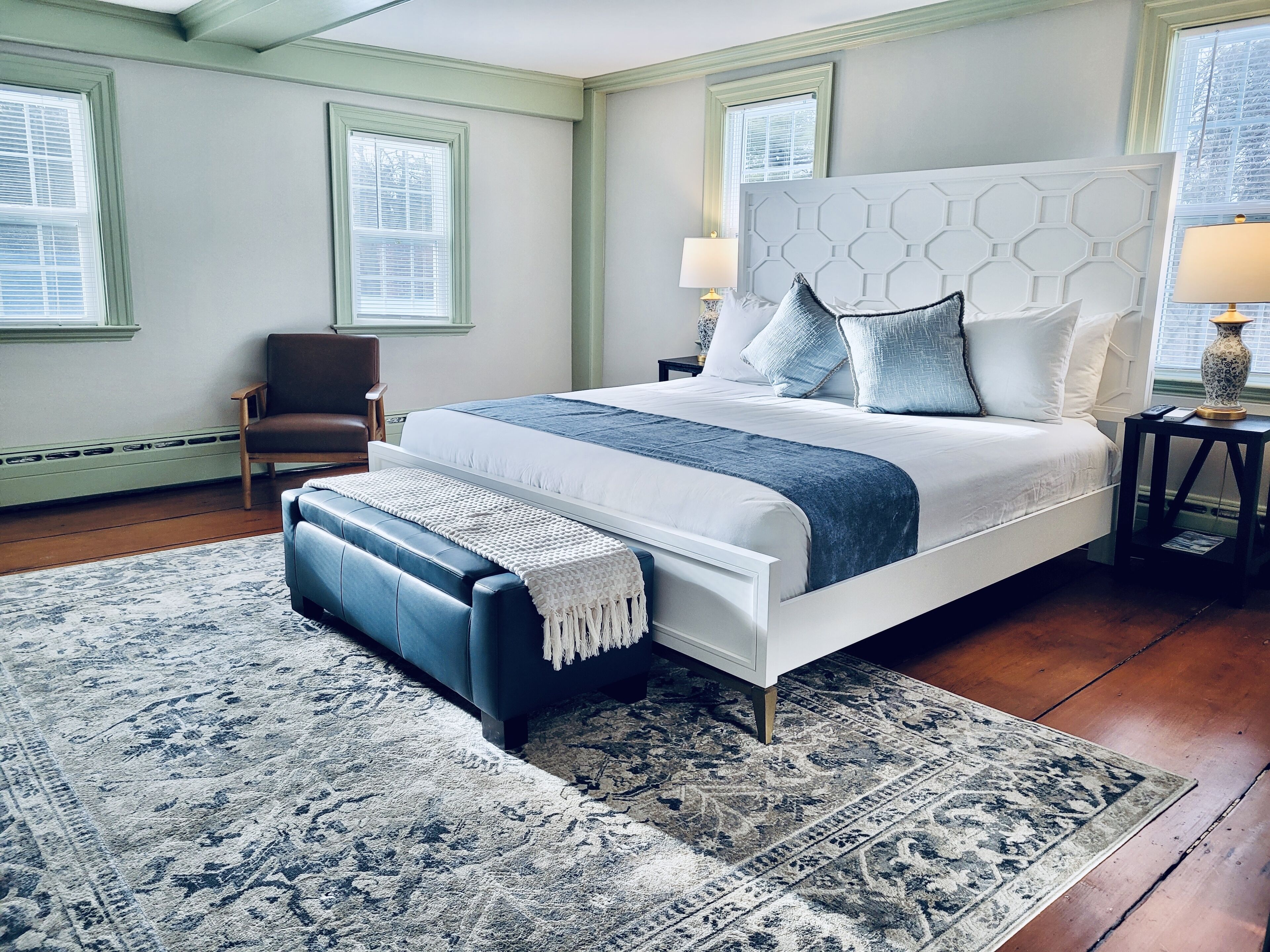 A bedroom with a large bed, a chair, a nightstand, and a window.