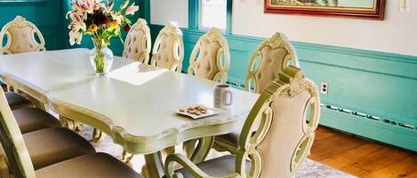 A dining room with a white table, cream chairs, and a teal accent wall.