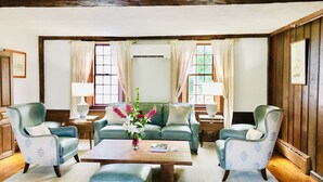 Een klassieke zithoek met een groene bank, twee fauteuils, een houten salontafel en een bloemenvaas.