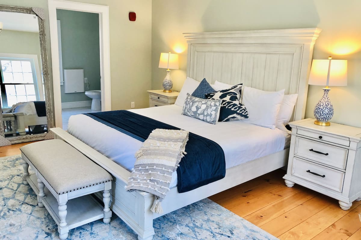 A neatly arranged bedroom with a large bed, bedside tables, a bench, and a mirror.