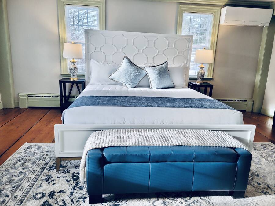 A bedroom with a large bed, two bedside tables, a blue bench, and a patterned rug.
