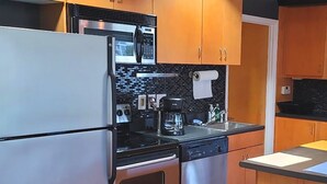 A compact kitchen with stainless steel appliances, wooden cabinets, and a black backsplash.