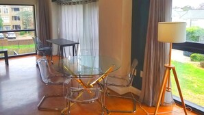A modern room with a glass table and chairs, a standing lamp, and a view of the outside.