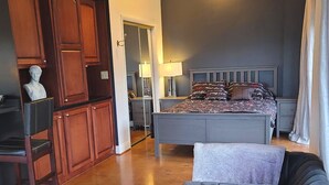 A bedroom with a bed, a chair, a desk, and a bust on the left.