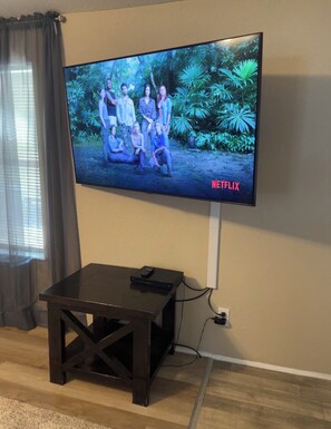 A television mounted on a wall with a remote control on a small table in front. - “Divers Inn” on The Rainbow River (Dunnellon)