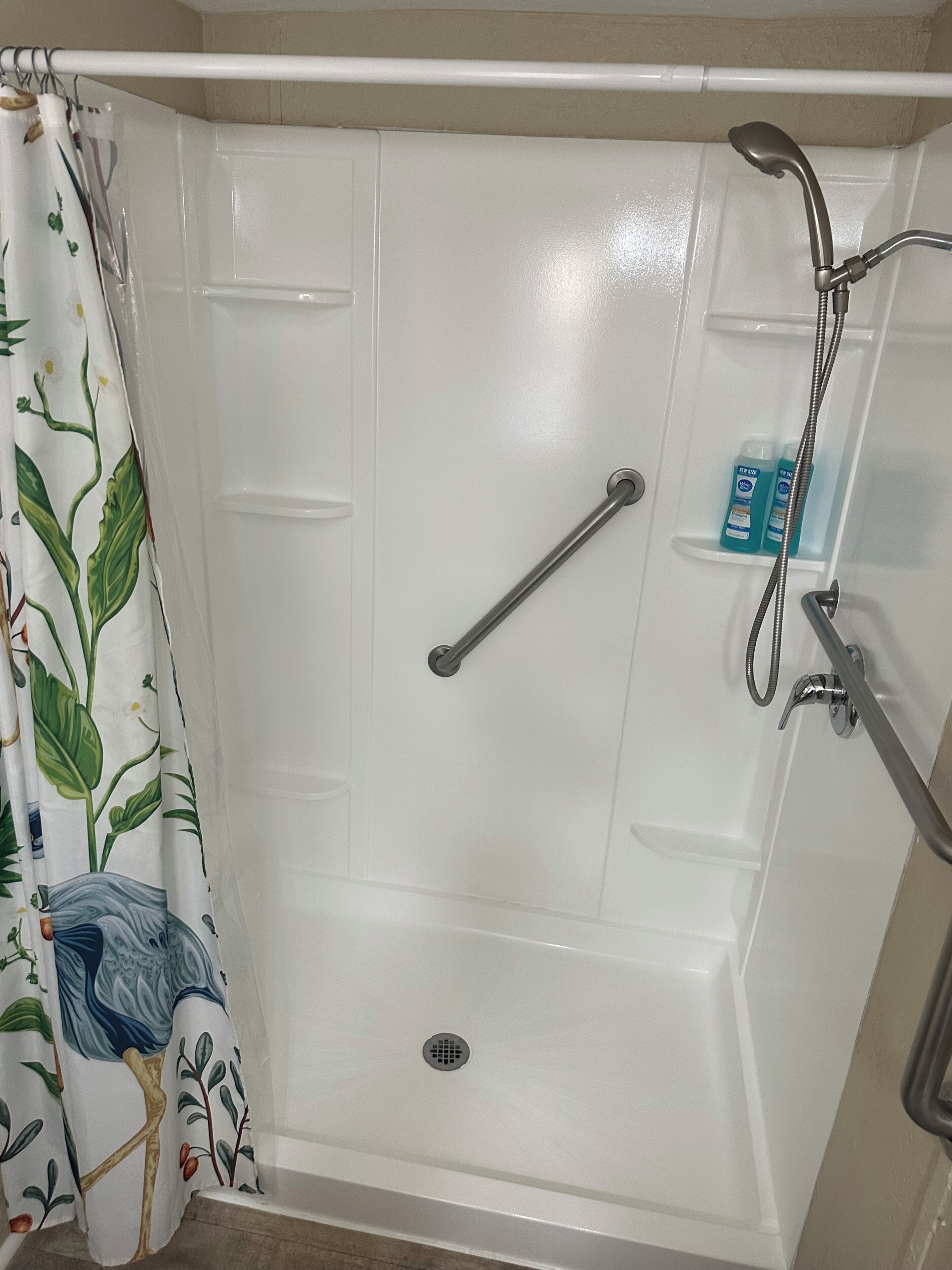 A walk-in shower with a grab bar, showerhead, and a shelf with toiletries.