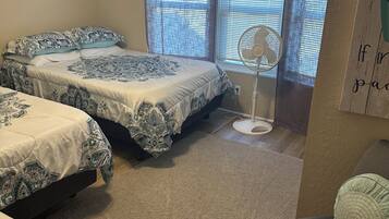 A bedroom with two beds, a ceiling fan, and a window with blinds.