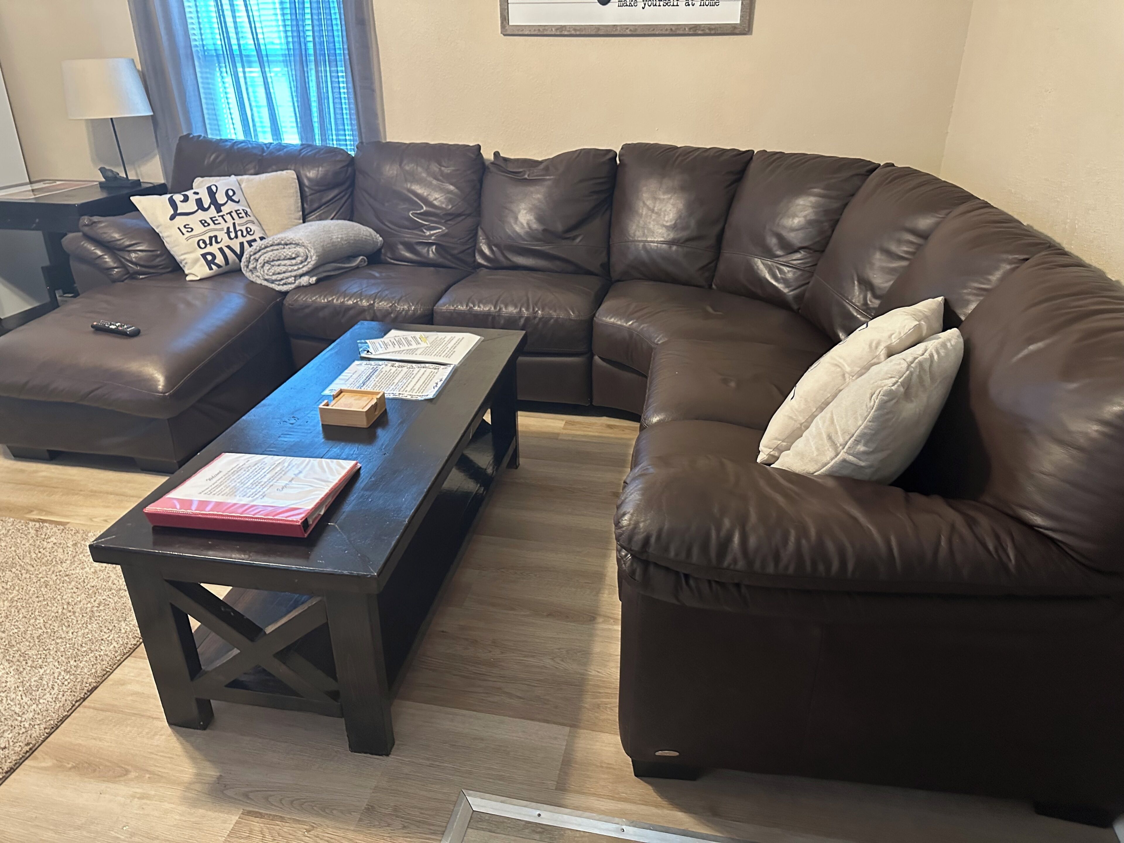 A living room with a brown leather sectional sofa, a wooden coffee table, and a small ottoman.