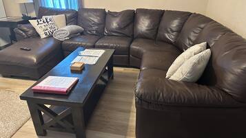 A living room with a brown leather sectional sofa, a wooden coffee table, and a small ottoman.