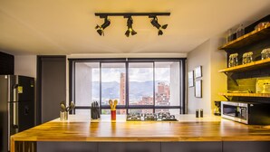 Une cuisine moderne dotée d’un grand îlot central, d’appareils électroménagers en acier inoxydable et offrant une vue sur la ville grâce à de grandes fenêtres.