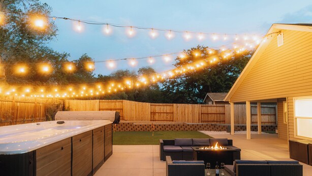 An outdoor patio with a hot tub, seating area, and string lights.