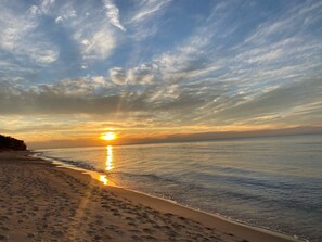 A beach with footprints leading to the water, a sunset in the background, and a clear sky.