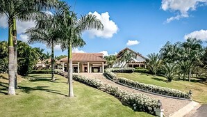 Un edificio grande su due piani, con tetto in tegole rosse, circondato da prati curati e palme.