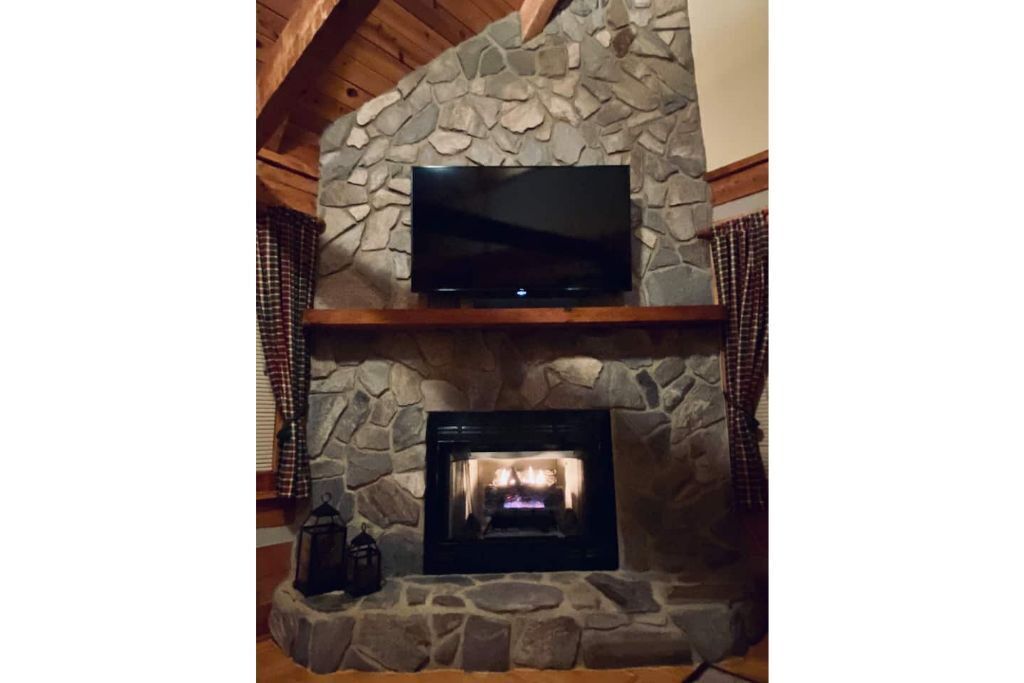 A stone fireplace with a television above it and a lit fire below.