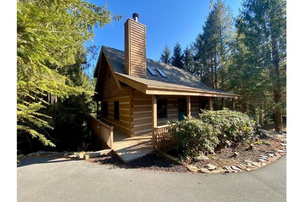 A log cabin with a chimney, a porch, and a small garden area.