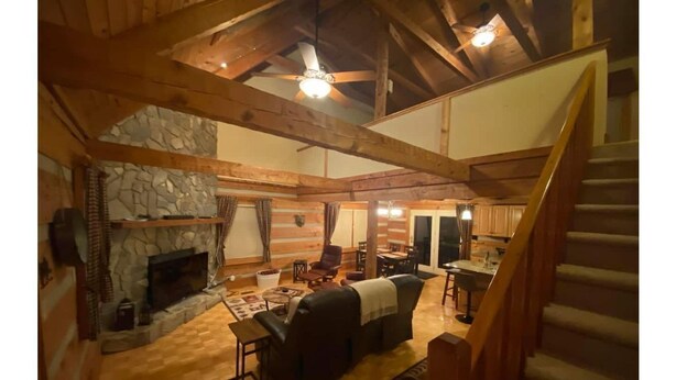 Ett rymligt vardagsrum i loftstil med en steneldstad, träbjälkar och en trappa.